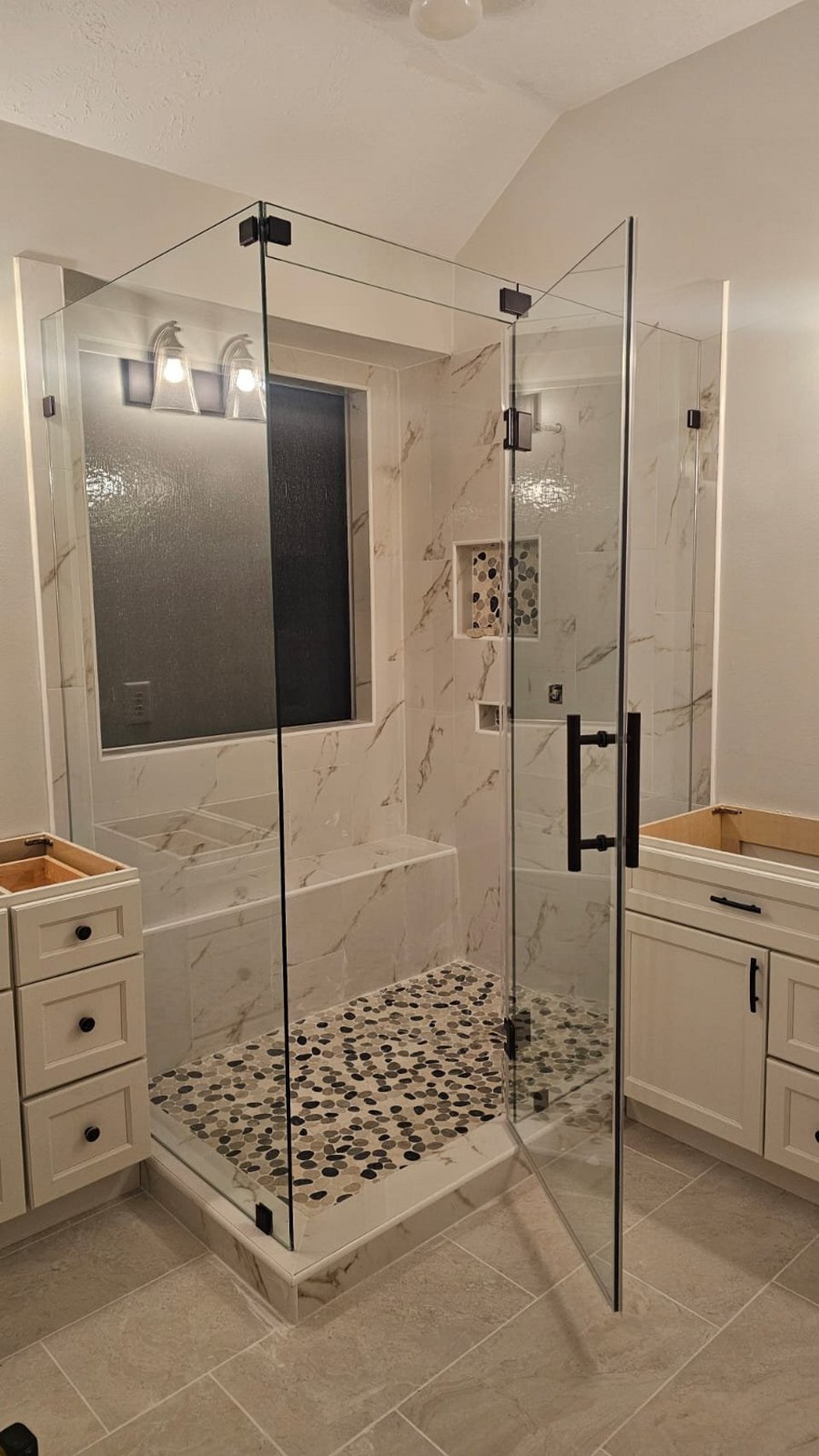 Glas Plus 90° angle over half walls example: clear glass with black hardware in a 90° corner, with a bench inside the shower