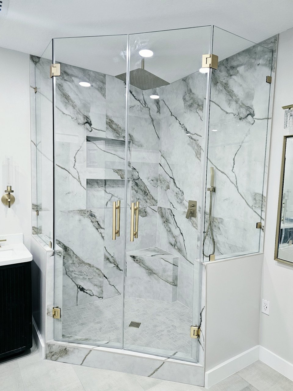 Glas Plus 90° angle over half walls example: clear glass with brush gold hardware mounted on half walls, in a marble bathroom