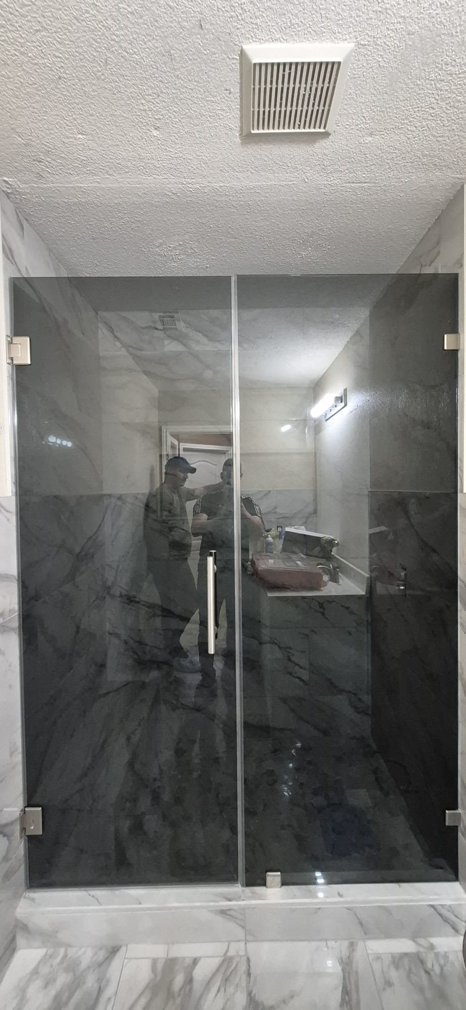 Hinged door with Grey glass (smoked grey), fixed panel and brush nickel hardware in a dark marble shower
