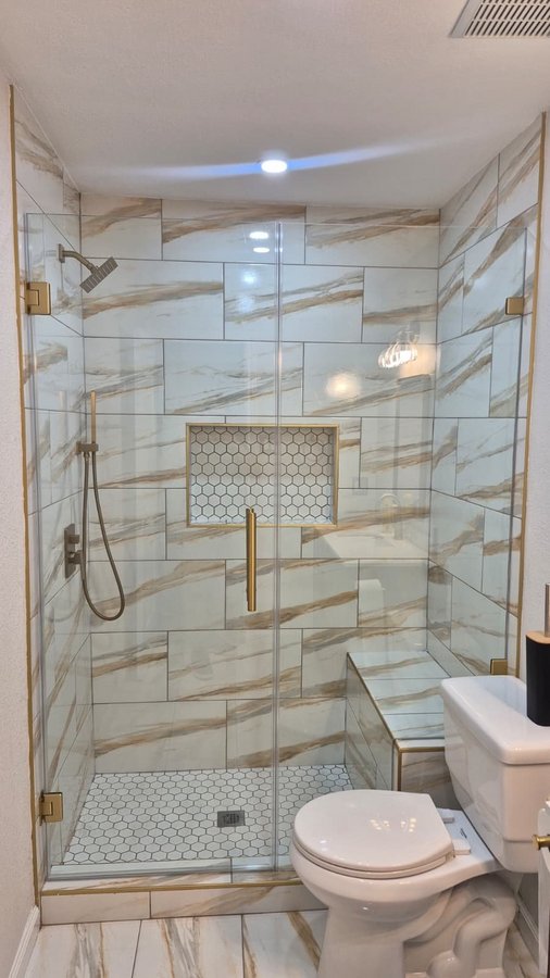 Glas Plus hinged door with wall example: wall-hinged door and fixed panel next to the shower tile bench, with brush gold hardware