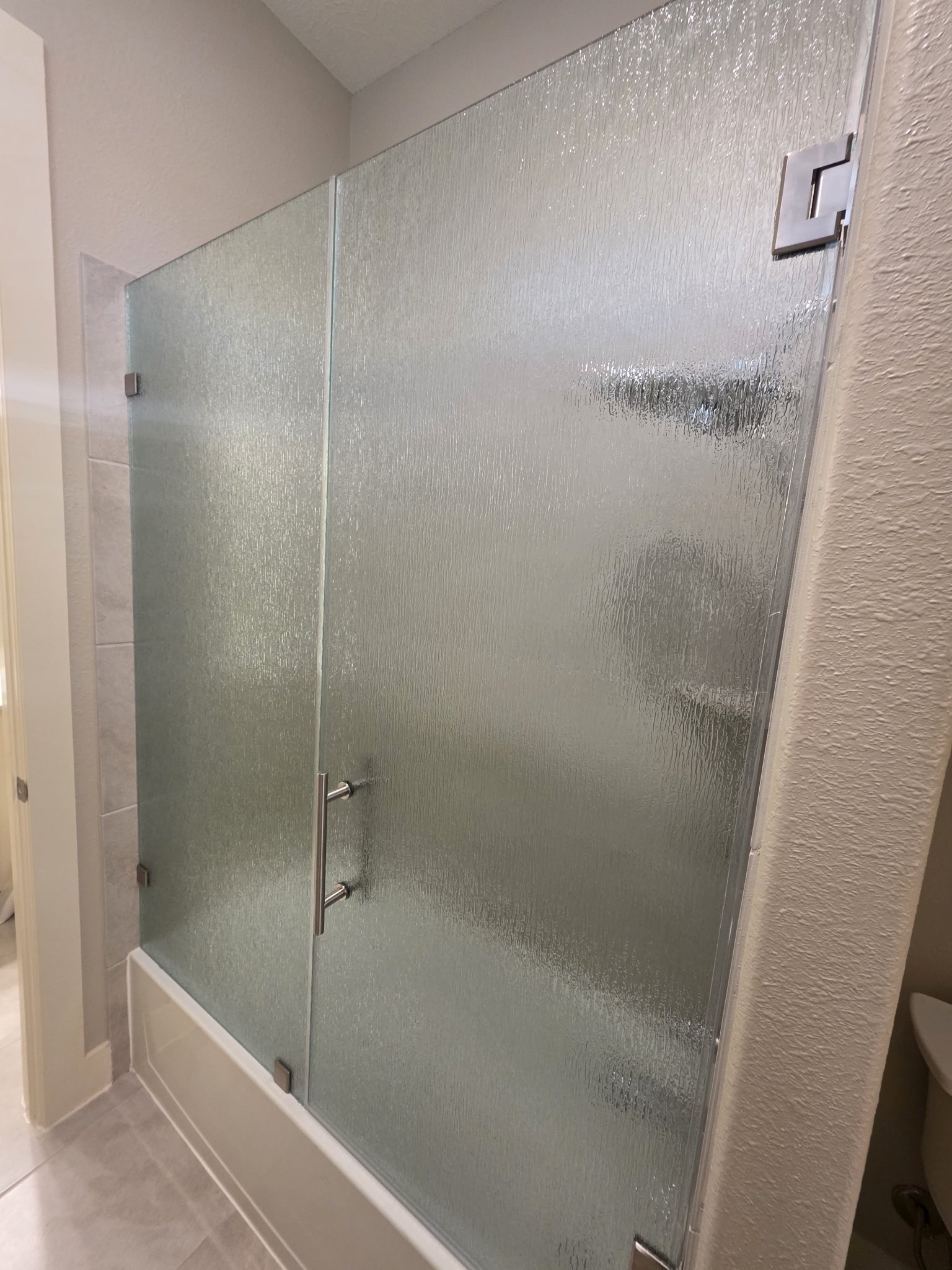 Hinged door with Rain glass (rain texture) and fixed panel over a tub, with brushed nickel hardware