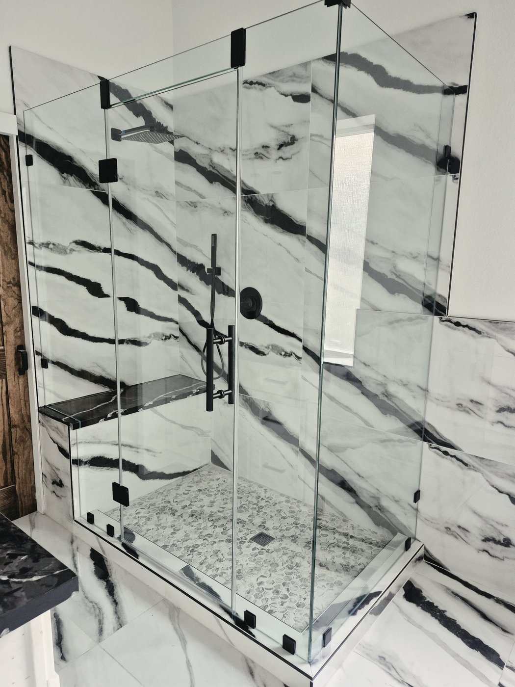 Glas Plus job: 90° angle with black hardware in a marble bathroom with black veining and an inside bench