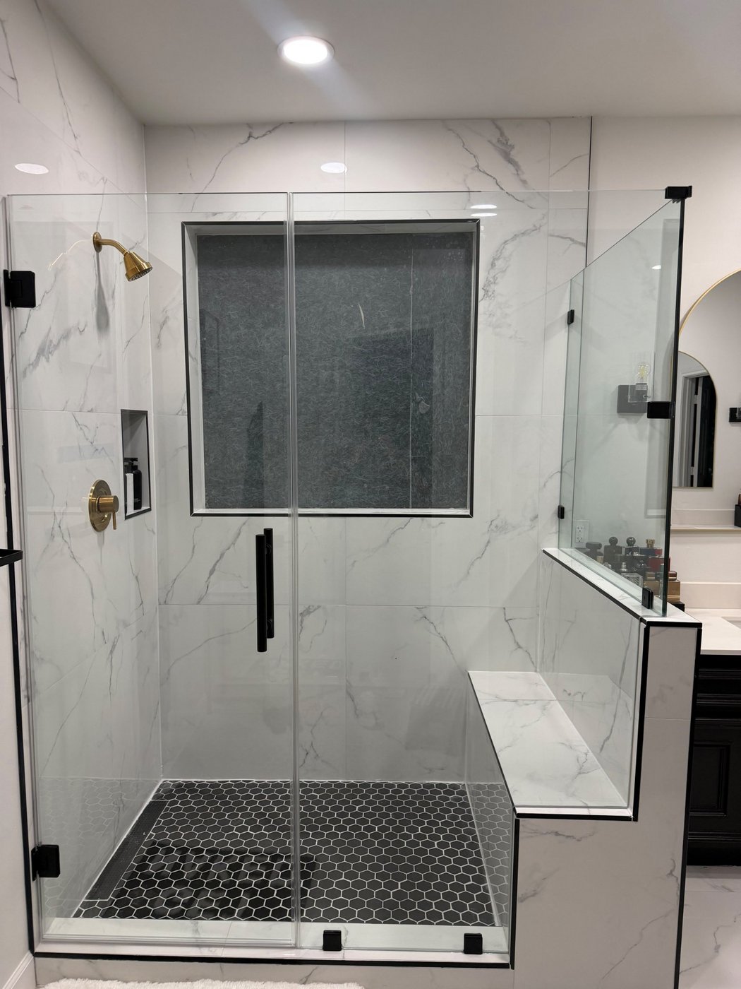 Glas Plus job: 90° angle with black hardware and the glass return over a half wall with a bench, in a marble shower