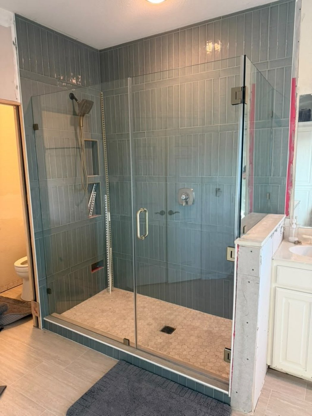 Glas Plus job: 90° angle with nickel hardware next to a half wall, in a greyish-blue tile shower