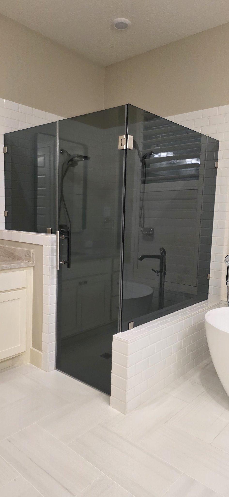 Glas Plus job: 90° angle shower with Grey glass (smoked grey) mounted on white tile walls, next to a tub