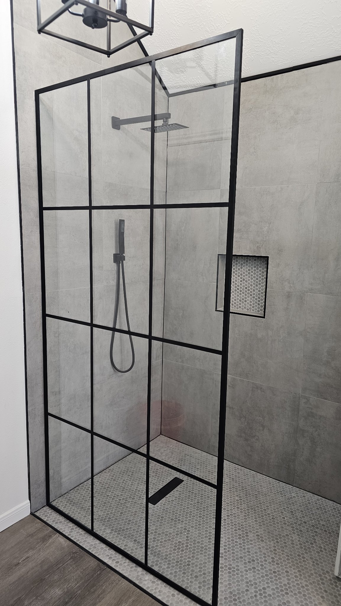 Glas Plus industrial-style grid panel reference photo: fixed clear glass panel with a black metal grid in an open shower