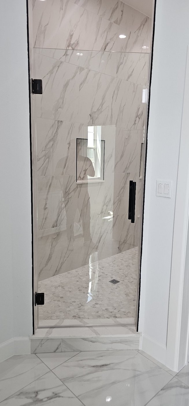 Single door with black hardware installed by Glas Plus in a white marble bathroom