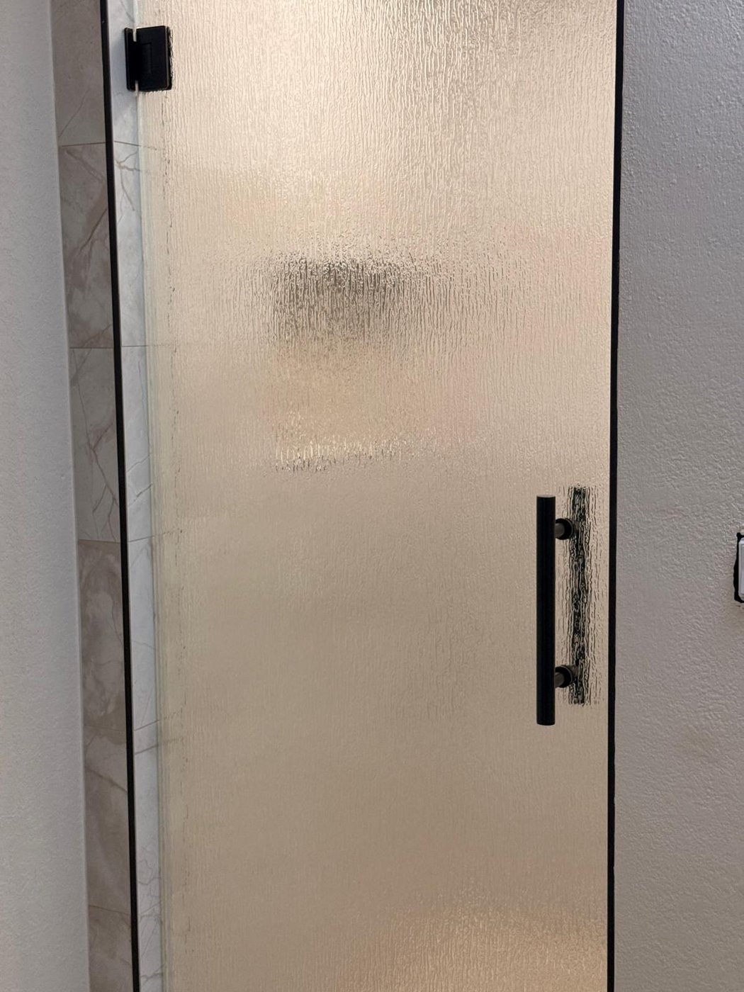 Single door with Rain glass (rain texture) and black handle installed by Glas Plus