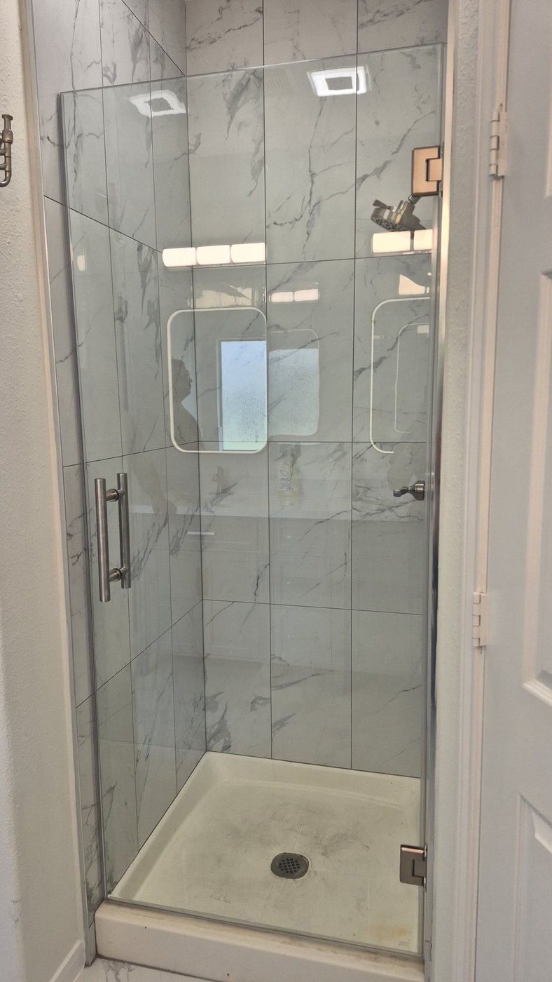 Single door with brush nickel hardware installed by Glas Plus in a marble shower