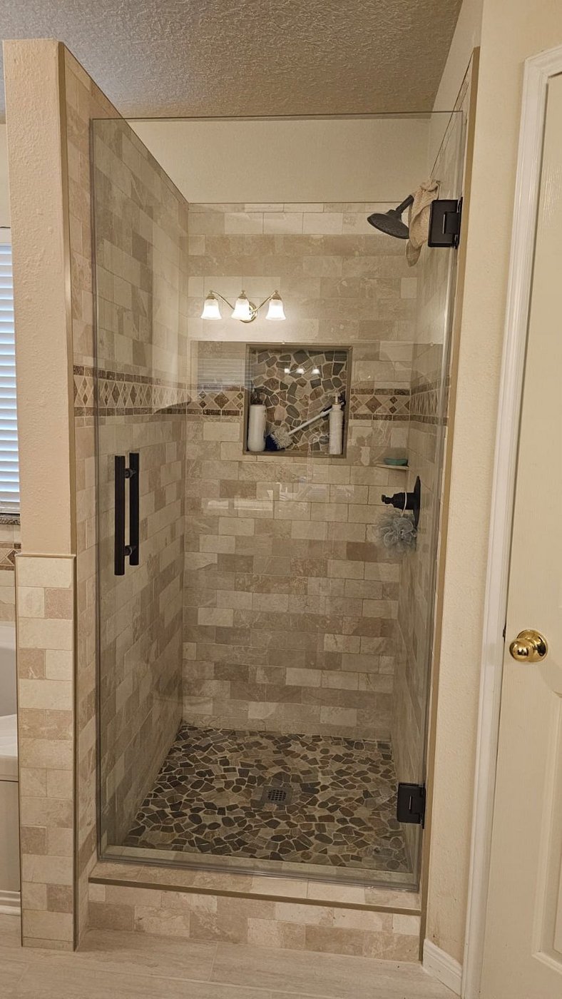 Single door with black hardware installed by Glas Plus in a beige tile shower