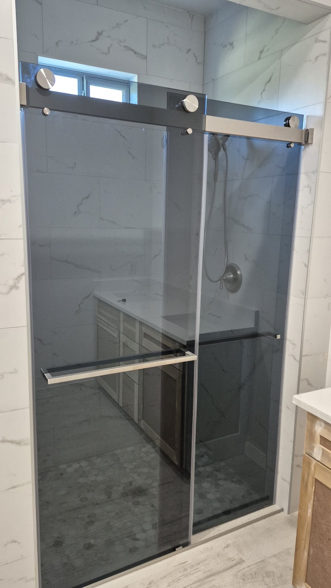 Double-door sliding with Grey glass (smoked grey) and brushed nickel track in a marble tile shower