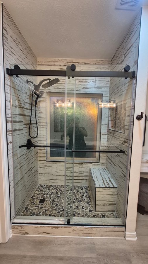Double-door sliding with black track and handle in a marble shower with a lit niche