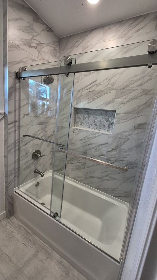 Double-door sliding with chrome track over a tub in a bathroom with a niche