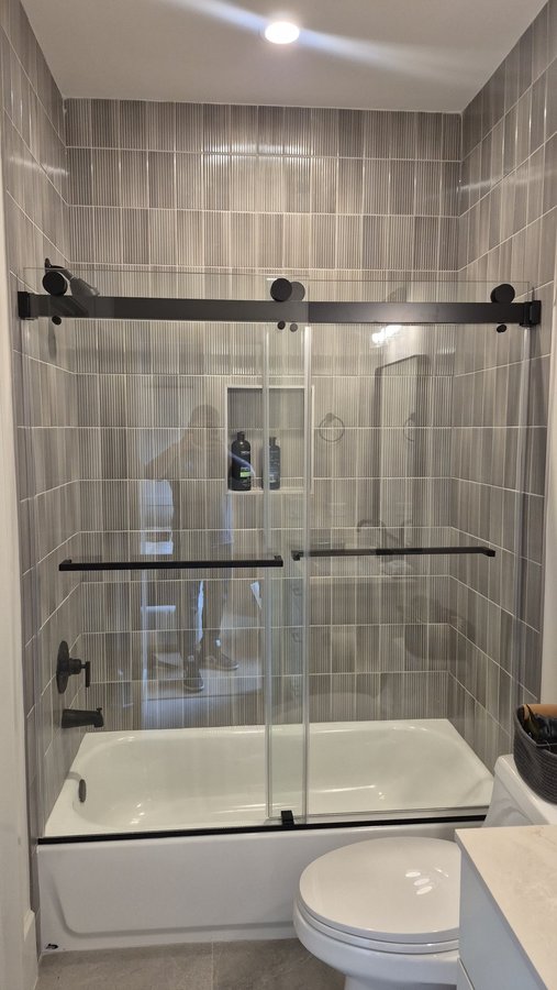 Double-door sliding with black track over a tub in a light bathroom with a niche