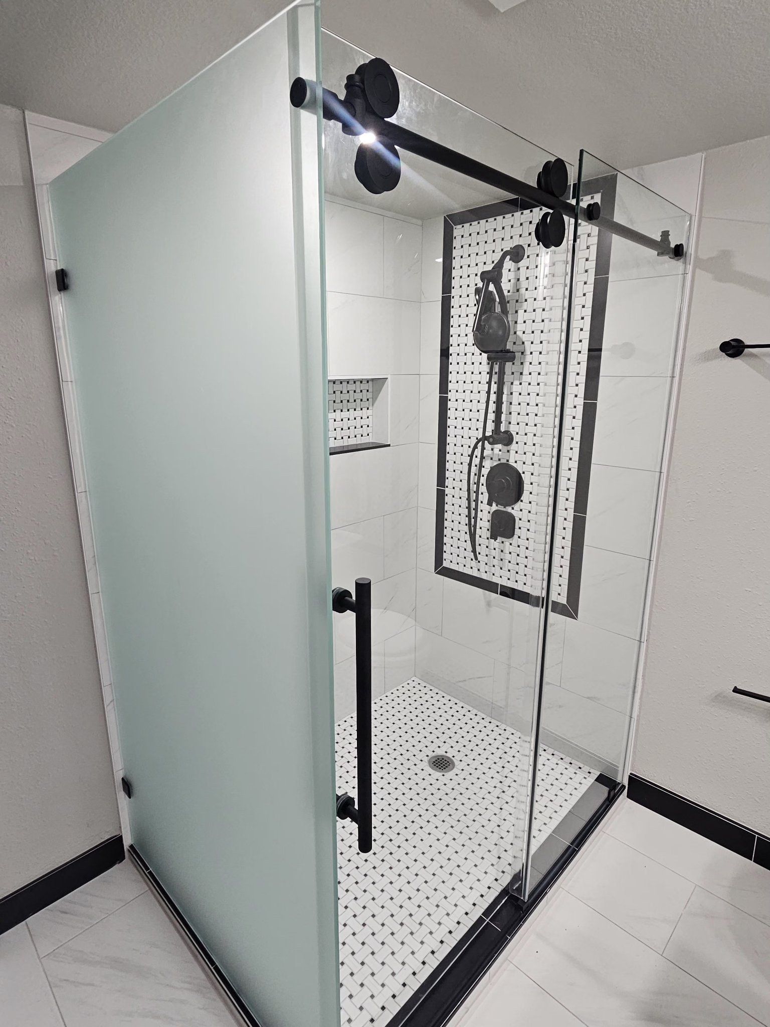 Sliding with return in Frosted glass (privacy) and black bar in a white tile shower with mosaic