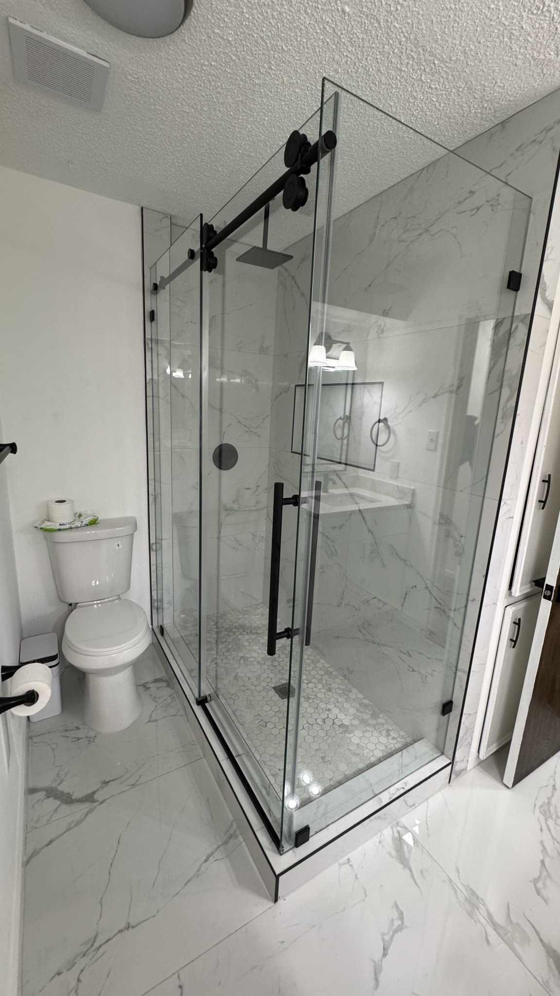 Sliding with return in clear glass with black track and hardware in a white marble shower