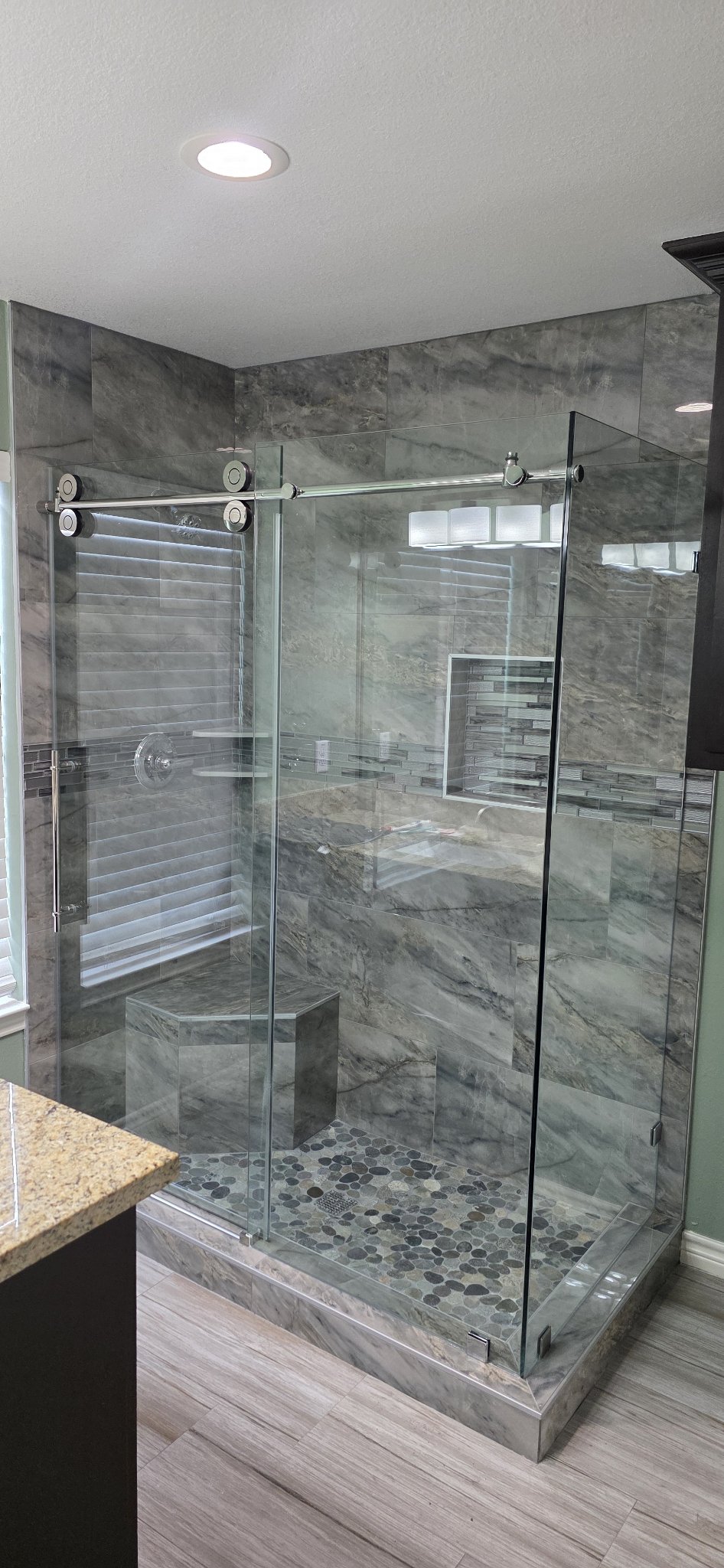 Sliding with return with a chrome track in a grey marble shower with a bench