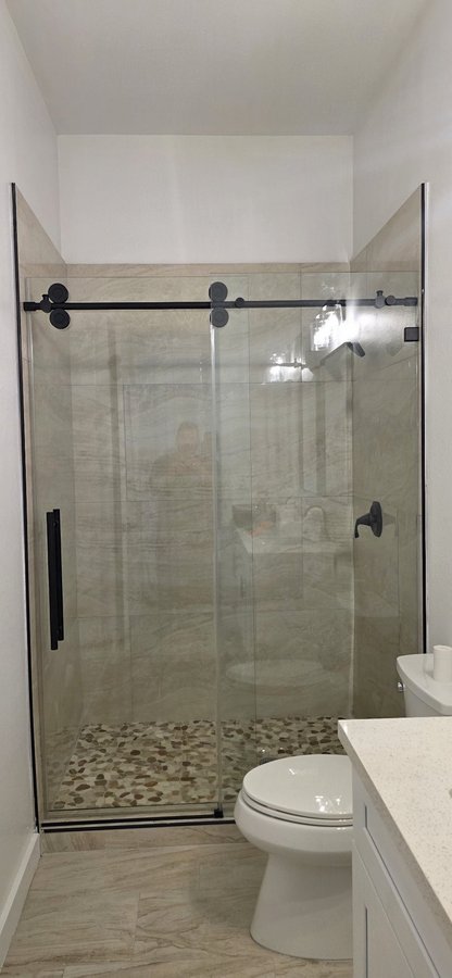 One-door sliding with black track and fixed panel in a white tile shower