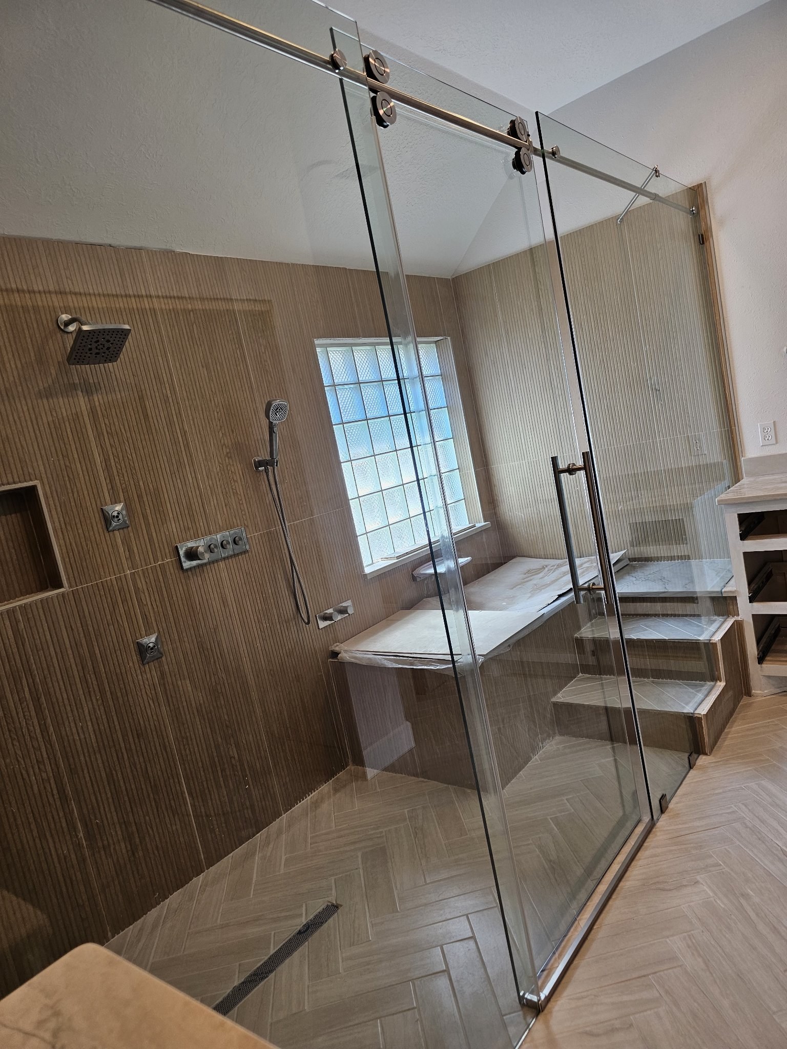 One-door sliding with fixed panel and brush nickel track in a large wood-look tile shower with a bench and glass block window