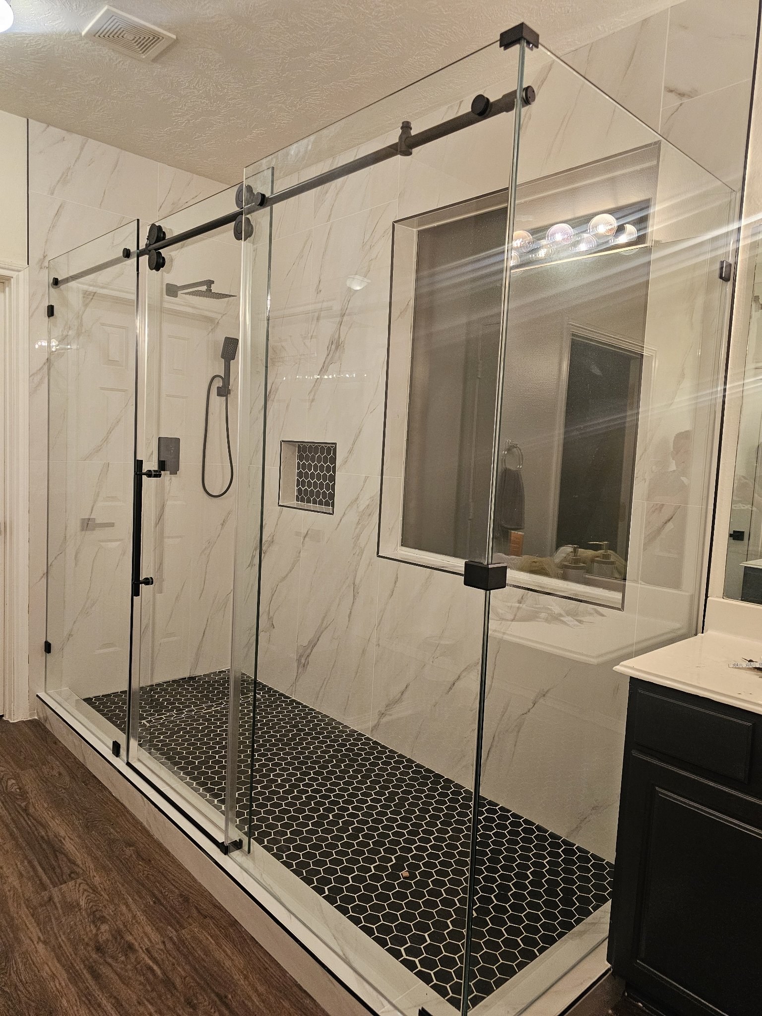 Sliding with side panels and center door, 90° angle with return and black hardware in a large white marble shower with an interior window
