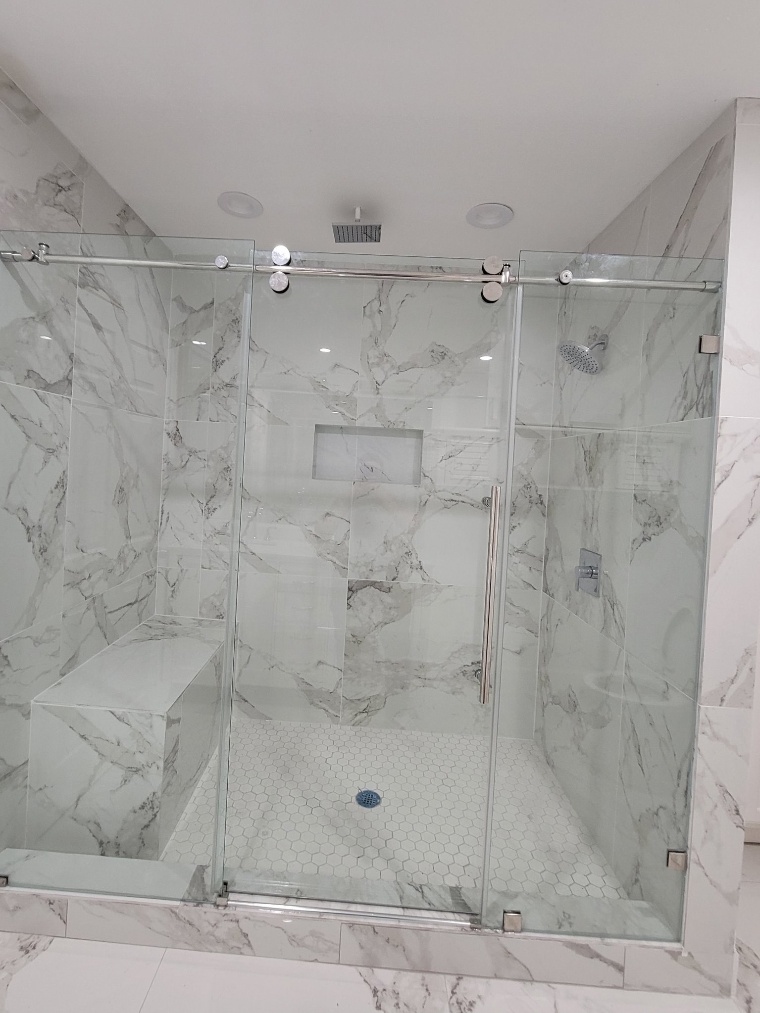 One-door sliding with fixed panel and chrome track in a marble shower with a bench and niche