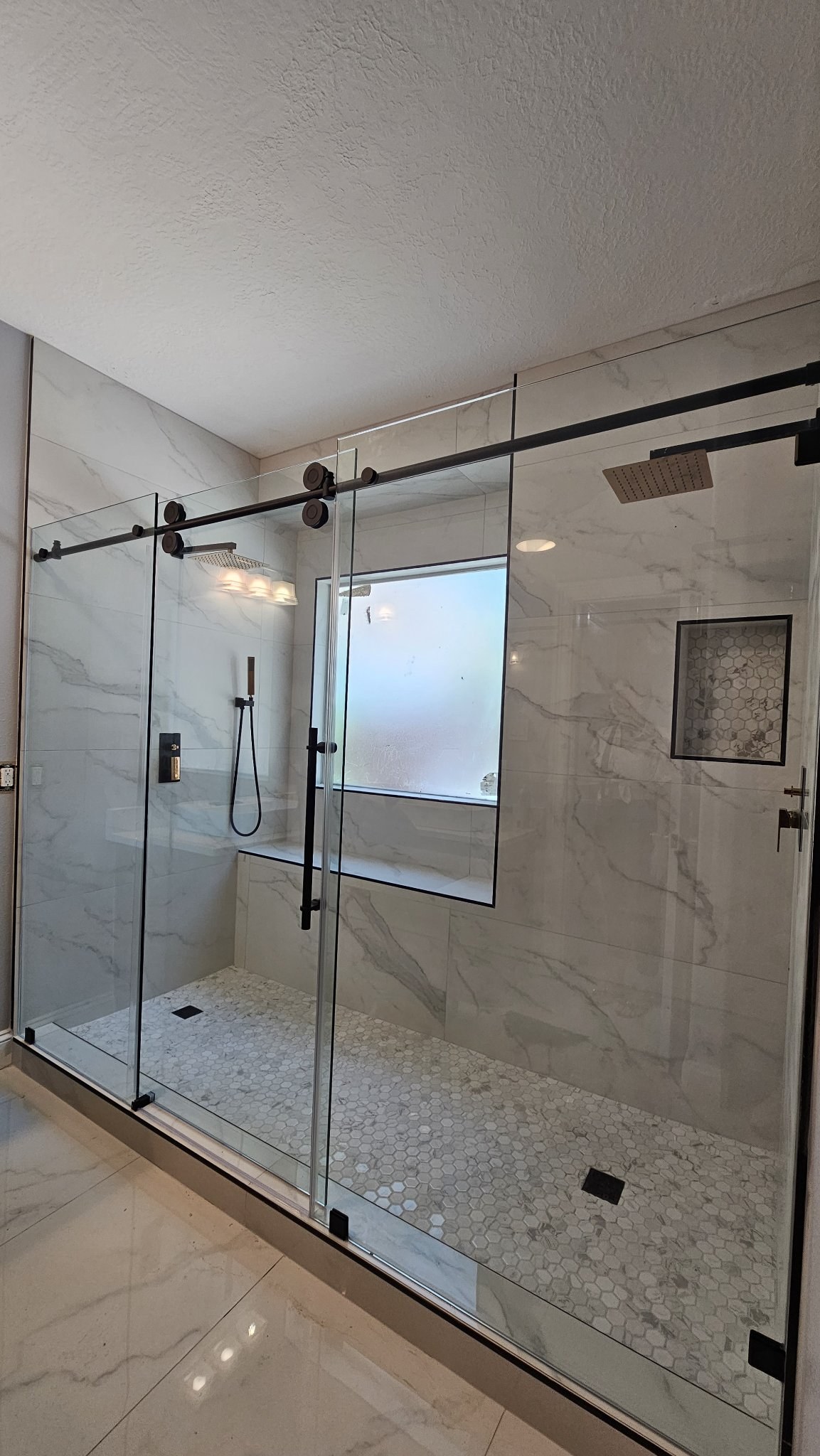Sliding with center door (fixed panel, door and fixed panel) with a black track in a white marble shower with a frosted window and two showers