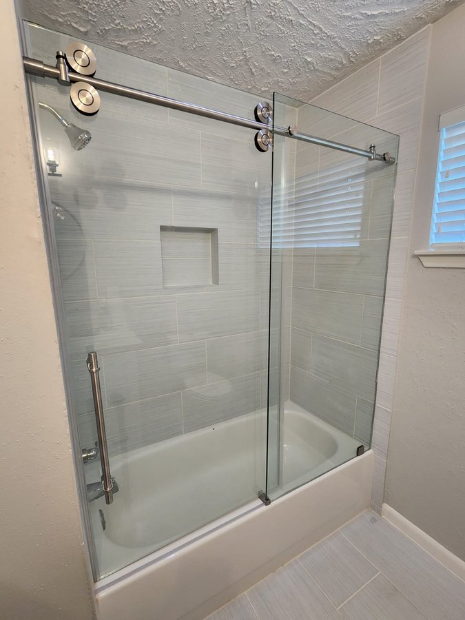 One-door sliding with round nickel track over a tub in a light grey tile bathroom